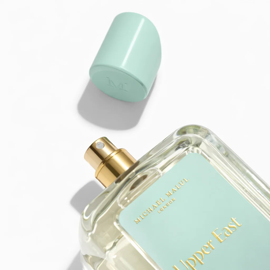Perfume bottle with gold cap and 'Upper East' label on a white background